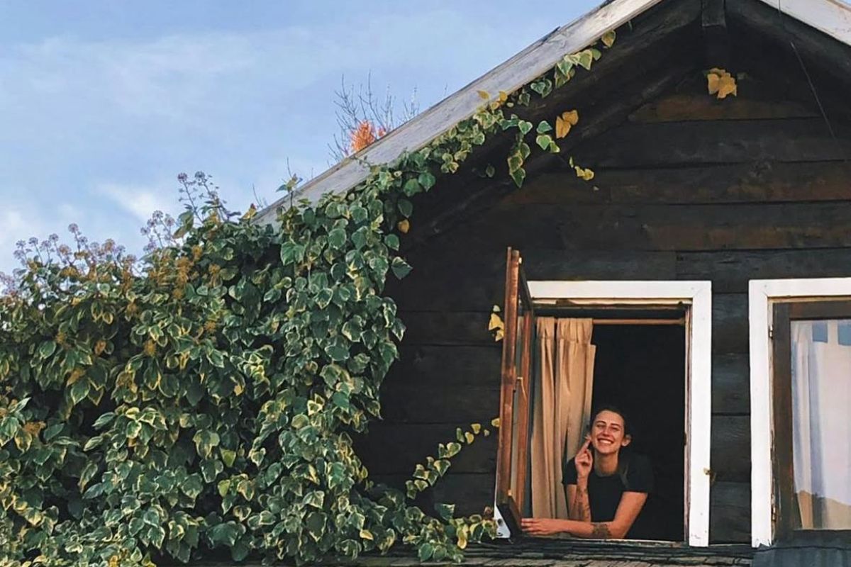 Ventana de madera con enredadera y huésped sonriente en El Oso Andaluz, hostel en San Martín de los Andes